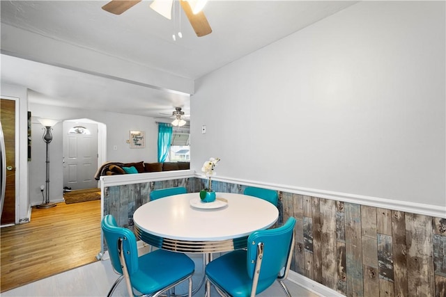 dining room featuring a ceiling fan, wood finished floors, and wood walls