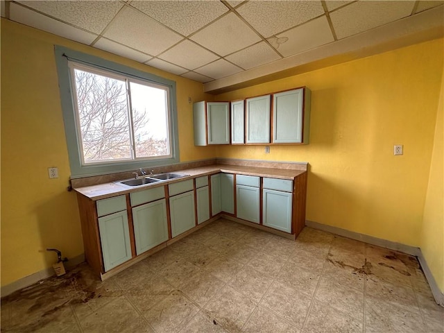 kitchen featuring a drop ceiling, a sink, and baseboards
