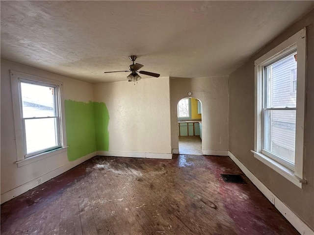 unfurnished room with wood-type flooring, arched walkways, ceiling fan, and baseboards