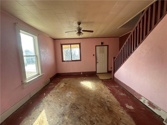 unfurnished living room with stairs, a ceiling fan, and baseboards