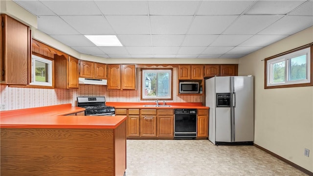 kitchen featuring appliances with stainless steel finishes, under cabinet range hood, a sink, brown cabinetry, and a paneled ceiling