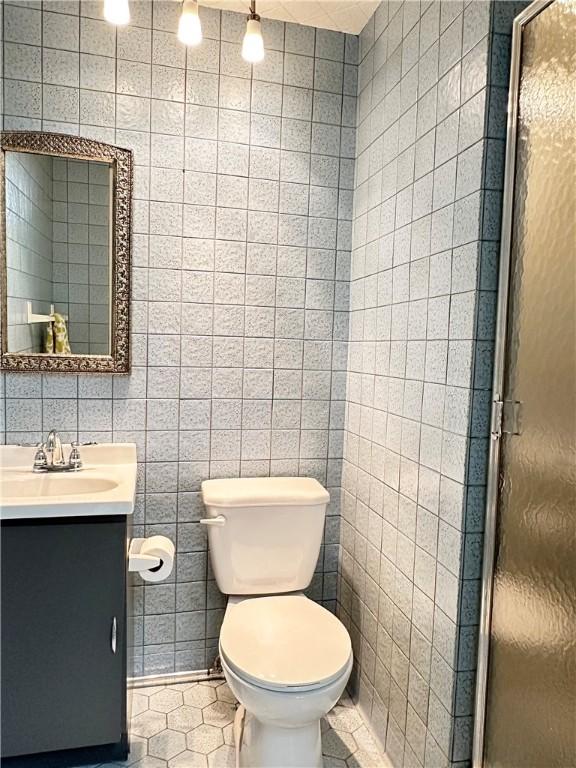 full bathroom with toilet, vanity, a shower stall, tile walls, and tile patterned floors