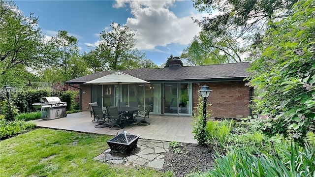 rear view of house featuring an outdoor fire pit, brick siding, a patio area, and a lawn