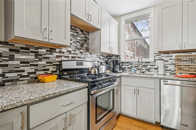 185 42nd St, Lawrenceville, PA 15201 - kitchen featuring stainless steel appliances, a sink, backsplash, light stone counters, and light wood-style floors