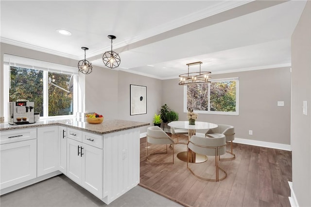 kitchen with baseboards, healthy amount of natural light, white cabinets, light stone counters, and crown molding