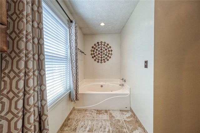 bathroom featuring a garden tub, a textured ceiling, and baseboards
