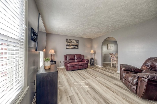 living area featuring arched walkways, light wood-style floors, a textured ceiling, and baseboards