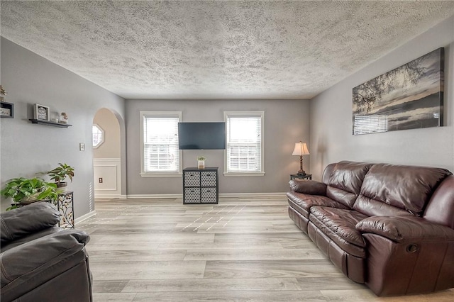 living room with arched walkways, light wood-style flooring, a textured ceiling, and baseboards