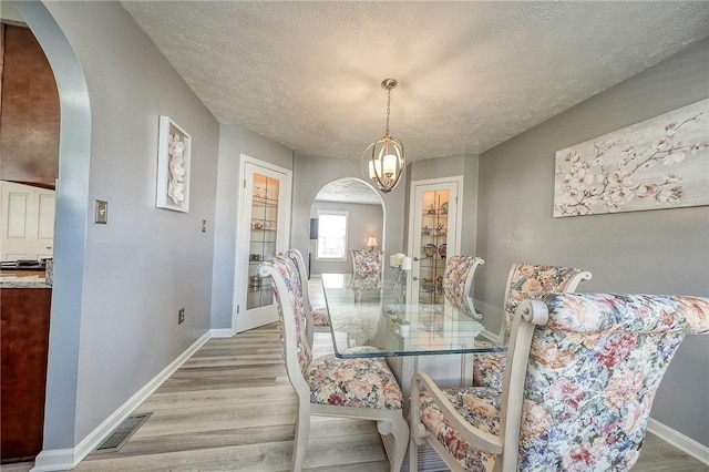 dining area featuring arched walkways, light wood finished floors, baseboards, and a textured ceiling