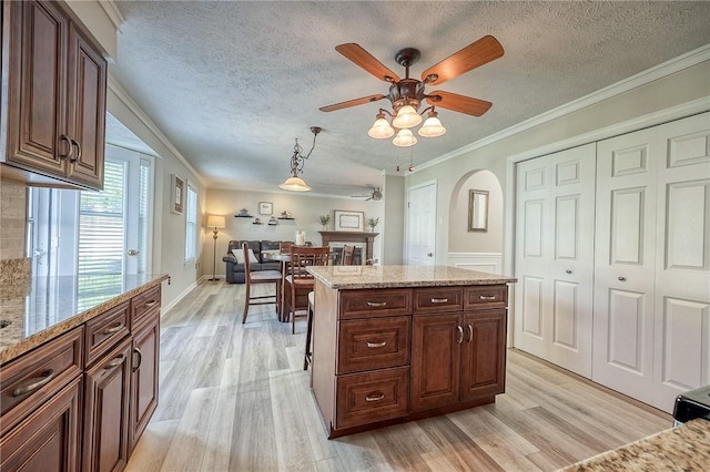 kitchen featuring light wood-style flooring, a ceiling fan, ornamental molding, arched walkways, and light stone counters