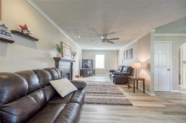 living room featuring arched walkways, wood finished floors, a ceiling fan, a textured ceiling, and crown molding