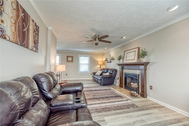 living room featuring wood finished floors, a textured ceiling, a ceiling fan, crown molding, and a high end fireplace