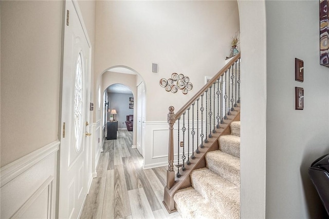 foyer entrance featuring arched walkways, light wood finished floors, wainscoting, a high ceiling, and a decorative wall