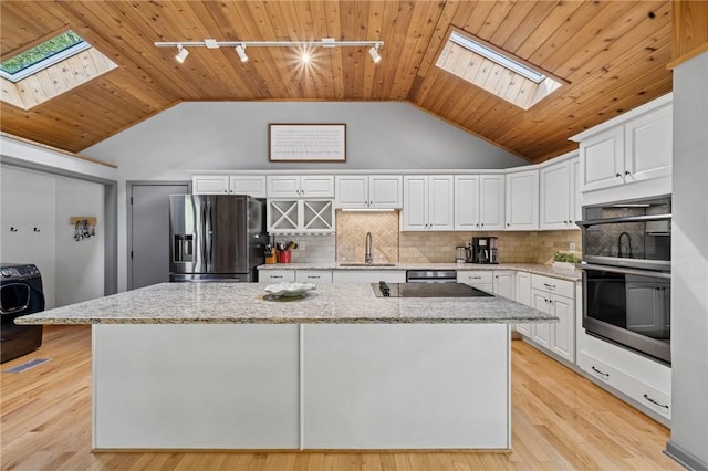 kitchen featuring a skylight, stainless steel fridge with ice dispenser, washer / clothes dryer, rail lighting, and lofted ceiling