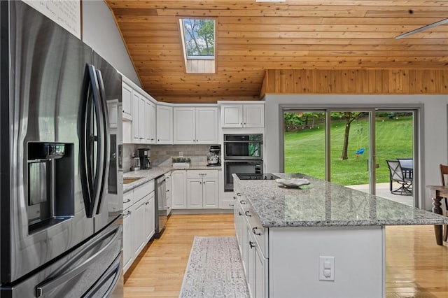 kitchen with appliances with stainless steel finishes, lofted ceiling, a kitchen island, white cabinetry, and tasteful backsplash