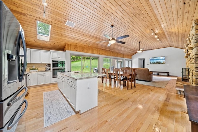 kitchen with stainless steel fridge, vaulted ceiling, double oven, white cabinets, and a kitchen island