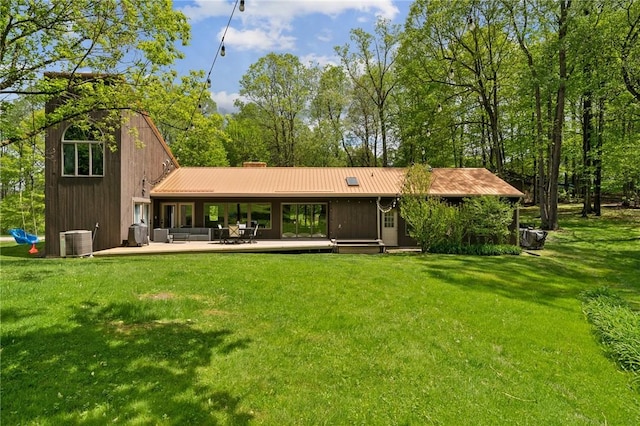 back of house featuring central air condition unit, a yard, metal roof, and a chimney