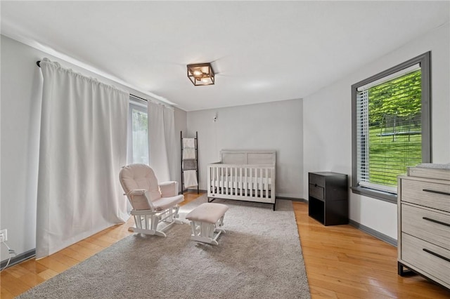 bedroom featuring multiple windows, light wood finished floors, and a nursery area