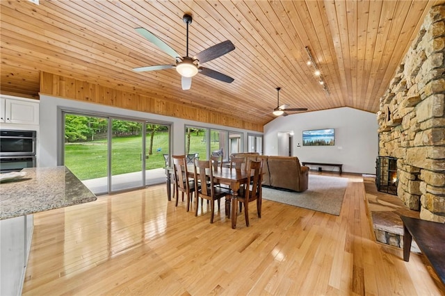 dining room with lofted ceiling, ceiling fan, wood ceiling, light wood-style flooring, and a fireplace