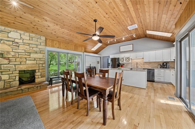 dining room with wooden ceiling, light wood-type flooring, a stone fireplace, a skylight, and ceiling fan