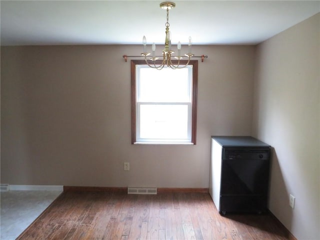 unfurnished dining area with a chandelier, wood finished floors, and baseboards