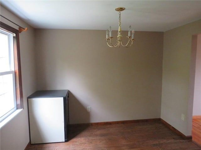 spare room featuring plenty of natural light, a chandelier, wood finished floors, and baseboards