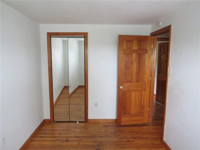 unfurnished bedroom featuring wood finished floors, baseboards, and a closet