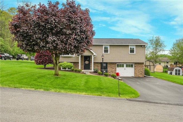 bi-level home with driveway, an attached garage, stone siding, a front lawn, and a shed
