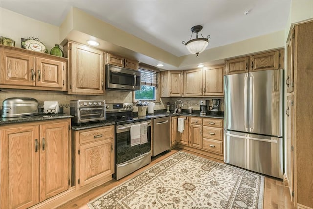 kitchen featuring appliances with stainless steel finishes, a sink, light wood finished floors, and decorative backsplash
