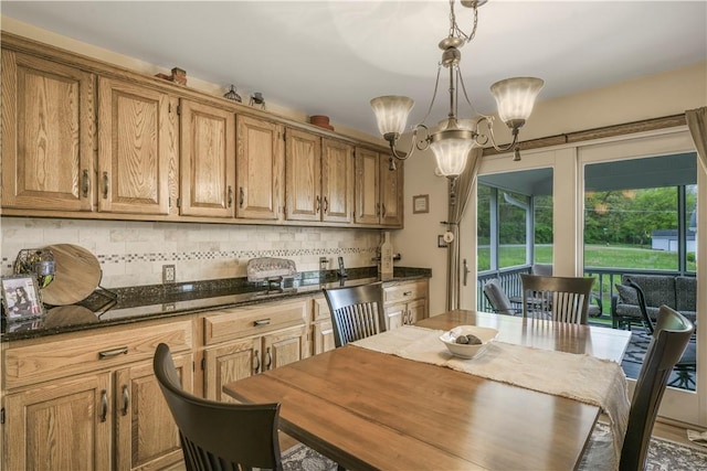 kitchen featuring a chandelier, decorative backsplash, dark stone counters, hanging light fixtures, and brown cabinets