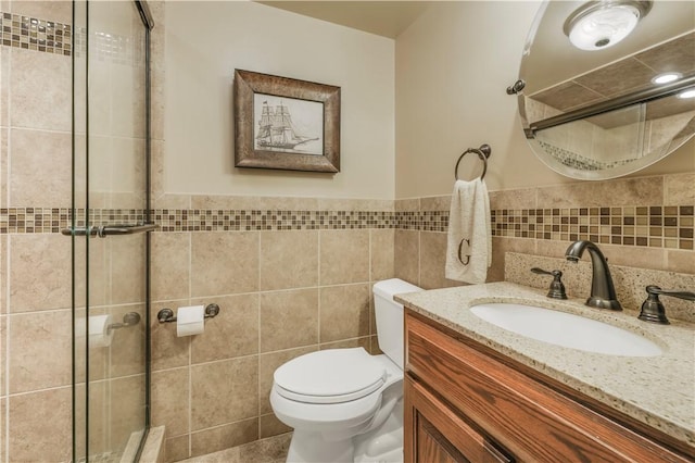 full bath featuring tile walls, a stall shower, toilet, vanity, and wainscoting