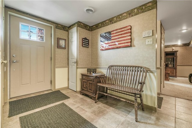 foyer featuring wallpapered walls, wainscoting, and stone finish floors