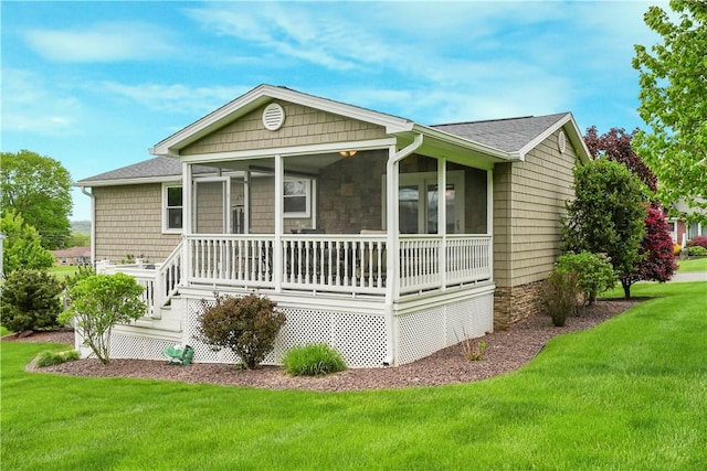 rear view of property featuring a sunroom, a yard, and roof with shingles