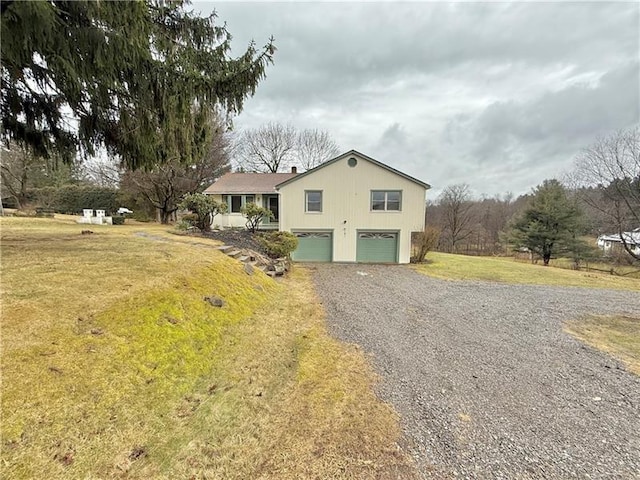 view of side of property featuring gravel driveway, a garage, and a lawn