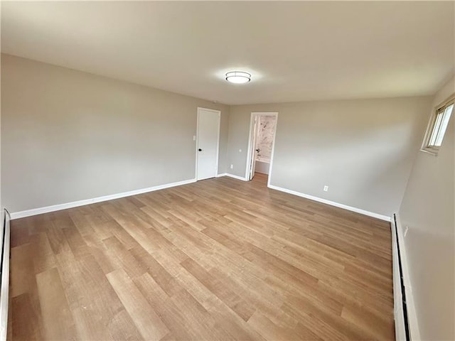 empty room featuring baseboards, light wood-style flooring, and a baseboard radiator