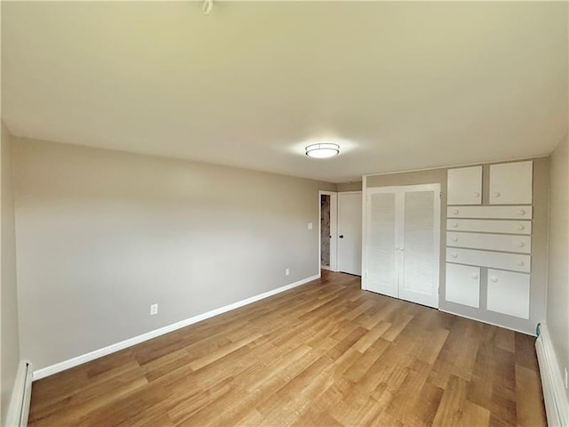 unfurnished bedroom featuring a baseboard radiator, a baseboard heating unit, baseboards, light wood-type flooring, and a closet