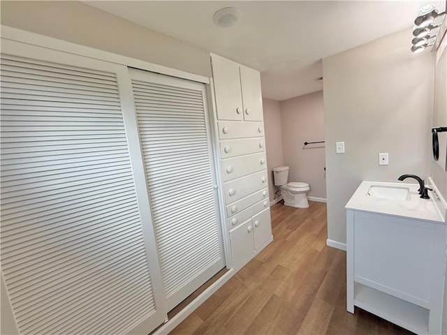 bathroom with toilet, wood finished floors, vanity, and baseboards