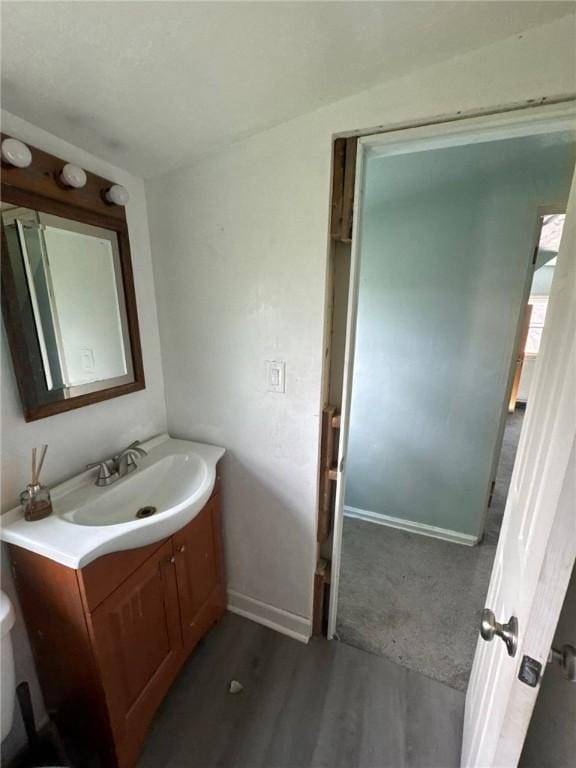 half bath featuring vanity, baseboards, and wood finished floors