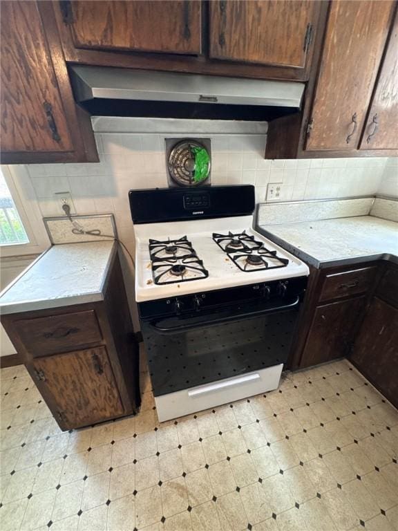 kitchen featuring range with gas stovetop, light floors, wall chimney range hood, and light countertops
