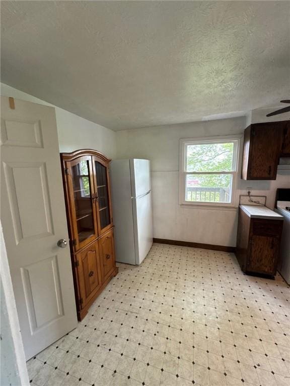kitchen with freestanding refrigerator, light flooring, baseboards, a textured ceiling, and range
