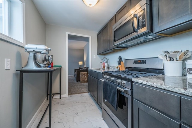 kitchen with appliances with stainless steel finishes, light marble finish floors, light stone countertops, a sink, and baseboards
