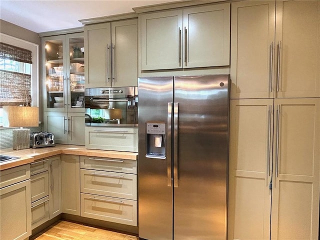 kitchen with stainless steel appliances, gray cabinets, butcher block countertops, light wood-style flooring, and glass insert cabinets