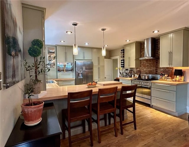 kitchen with stainless steel appliances, wall chimney range hood, gray cabinetry, wood counters, and a peninsula
