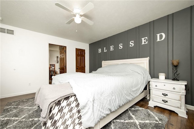 bedroom with dark wood-style floors, baseboards, a ceiling fan, and a decorative wall