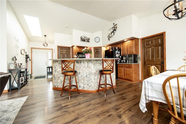 kitchen featuring brown cabinetry, dark wood-type flooring, an island with sink, a kitchen bar, and a skylight