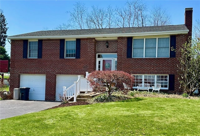 split foyer home with a garage, a front lawn, a chimney, asphalt driveway, and brick siding