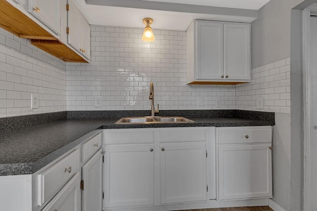 kitchen with a sink, dark countertops, white cabinetry, and backsplash