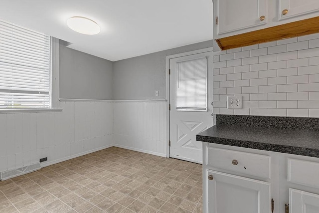 kitchen with dark countertops, backsplash, white cabinets, and a wainscoted wall