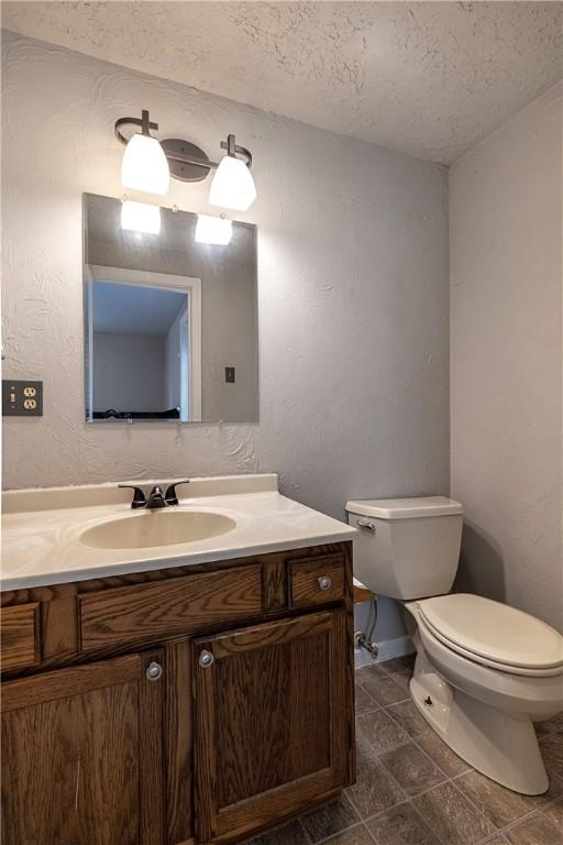 half bath with toilet, a textured ceiling, vanity, baseboards, and tile patterned flooring