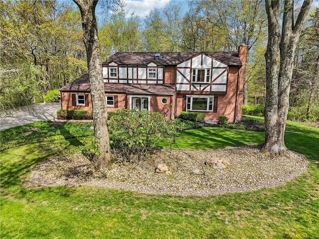 tudor home with a chimney, a front yard, brick siding, and driveway
